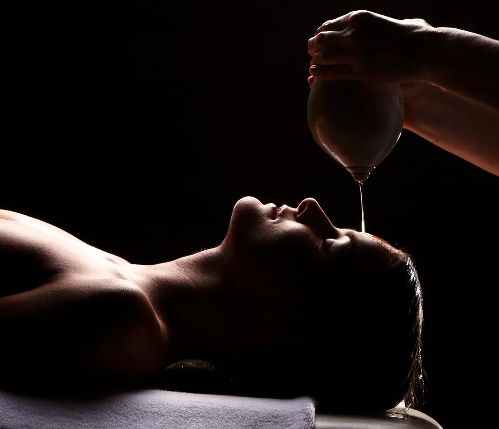 A thin thread of warm oil poured from a vessel onto the brow of a guest at rest