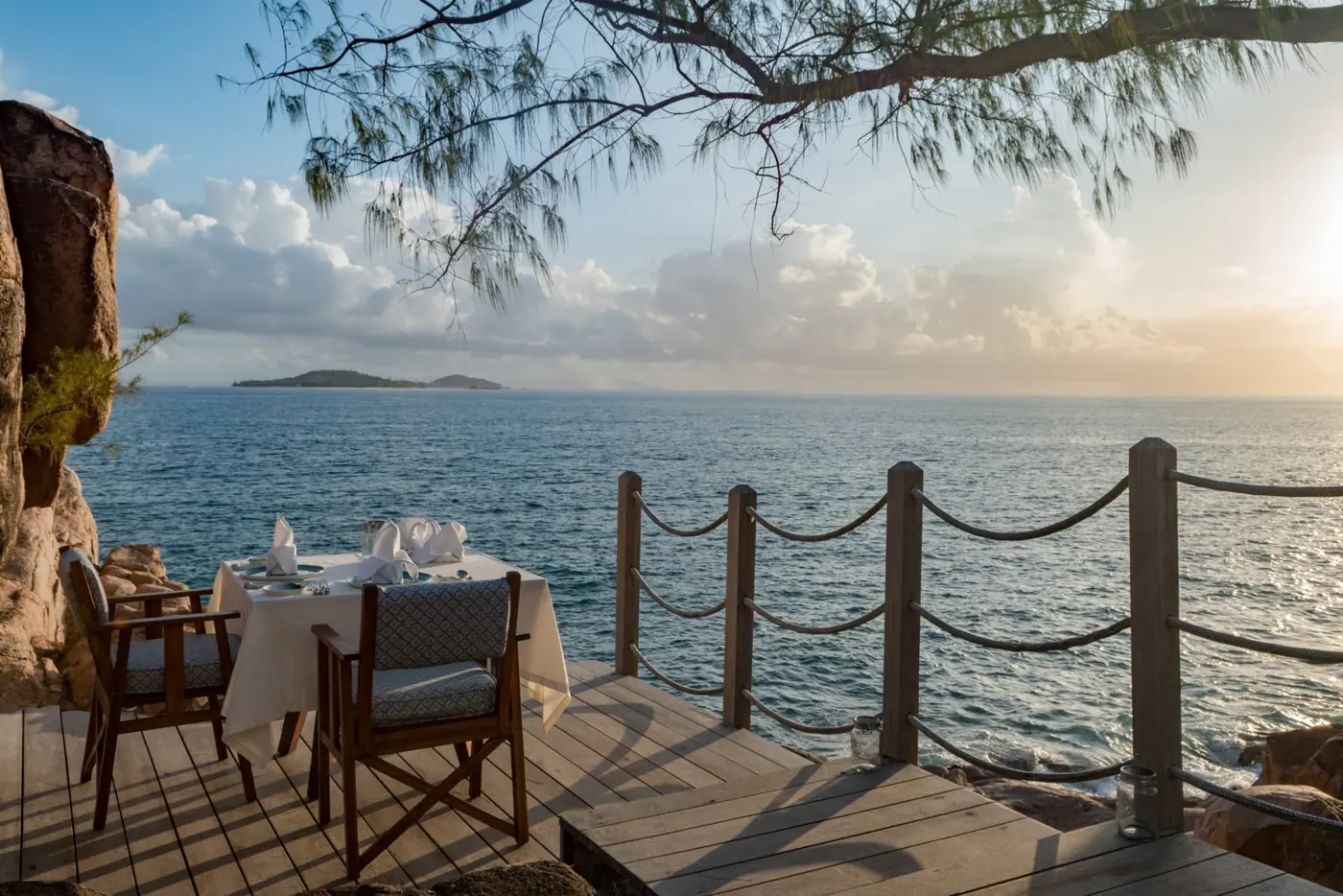 A table laid for dinner on a deck above the sea at dusk