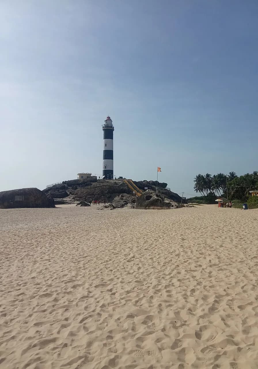 The black-and-white Kaup lighthouse on its rocks above a wide pale-sand beach, twenty minutes from SeaSwara.